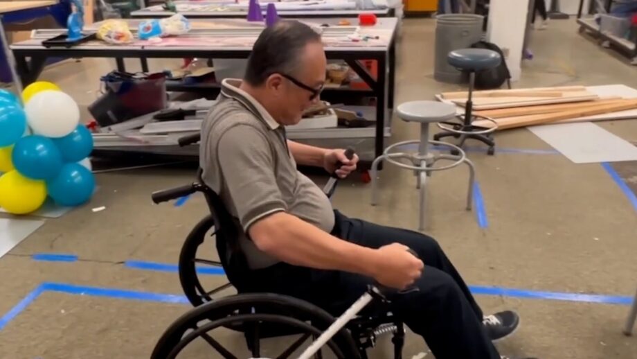A man in a wheelchair using a 3D printed lever to move forward.