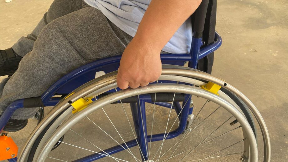 A customised wheelchair with an adapted rim positioned closer to the user’s hands and 3D-printed components supporting a wooden foot platform for improved comfort and control.