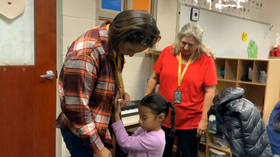 A young girl who is blind reaching up and feeling a person's lanyard.