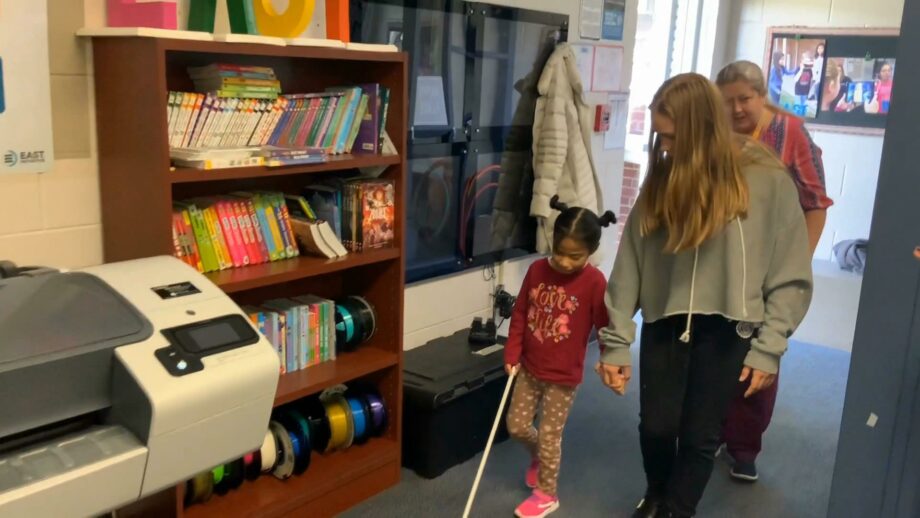 A person holding the hand of a young girl with a cane.