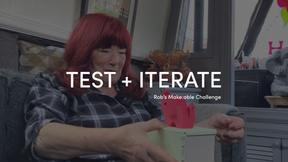 Make:able Champion, Cath, holding Pinchee - a 3D printed pinching game aimed at supporting users with arthritis. The title 'Test + Iterate' is overlaid in white bold text.
