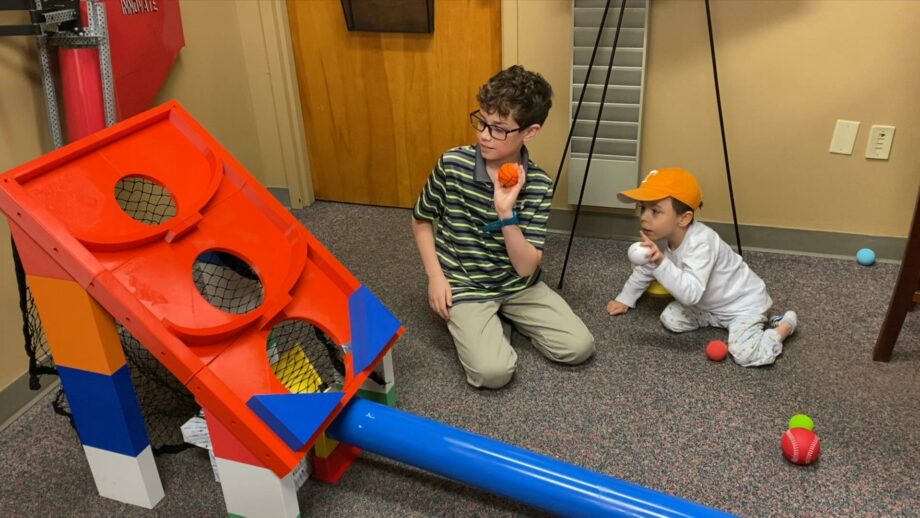 2 children playing with a 3D printed arcade ball game, which involves throwing balls into holes.