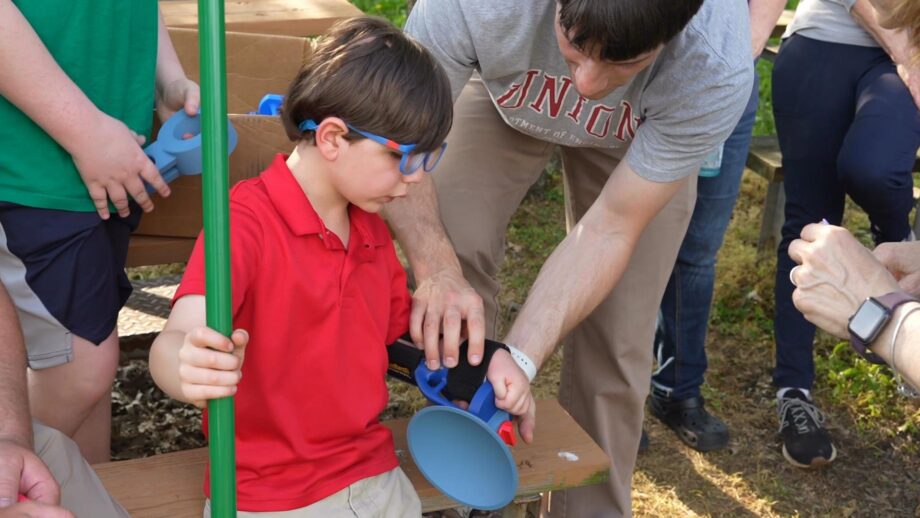 A boy wearing a 3D printed arm attachment that helps to catch balls.