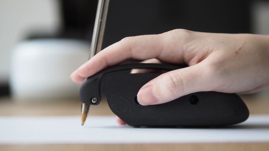 A hand resting on top of an assistive writing device that involves pressing down to write.