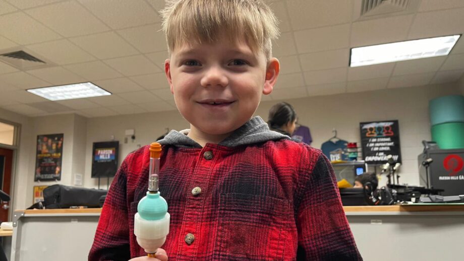 A boy holding a pencil with a 3D printed weight device on the end.