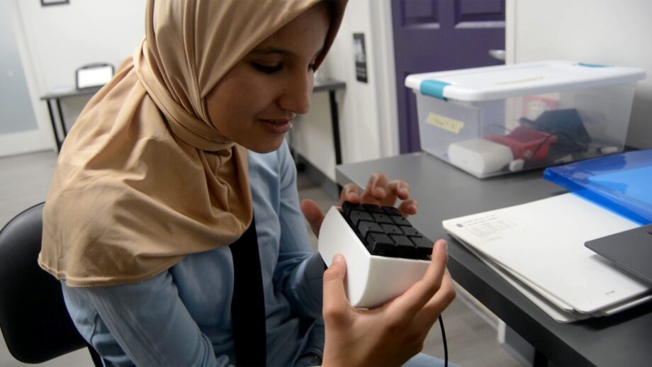 A girl with visual impairment holds the 3D-printed Touch Type braille keyboard, a compact tactile device designed to support accessible typing and communication.