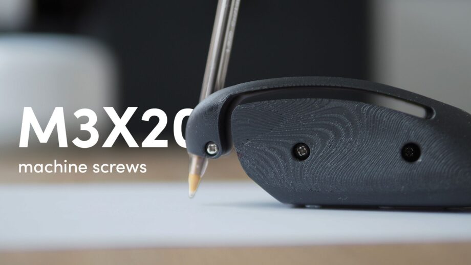 A DRAG assistive writing device displayed with the text “M3×20 machine screws” overlaid, highlighting the use of standard, easily sourced fixings.