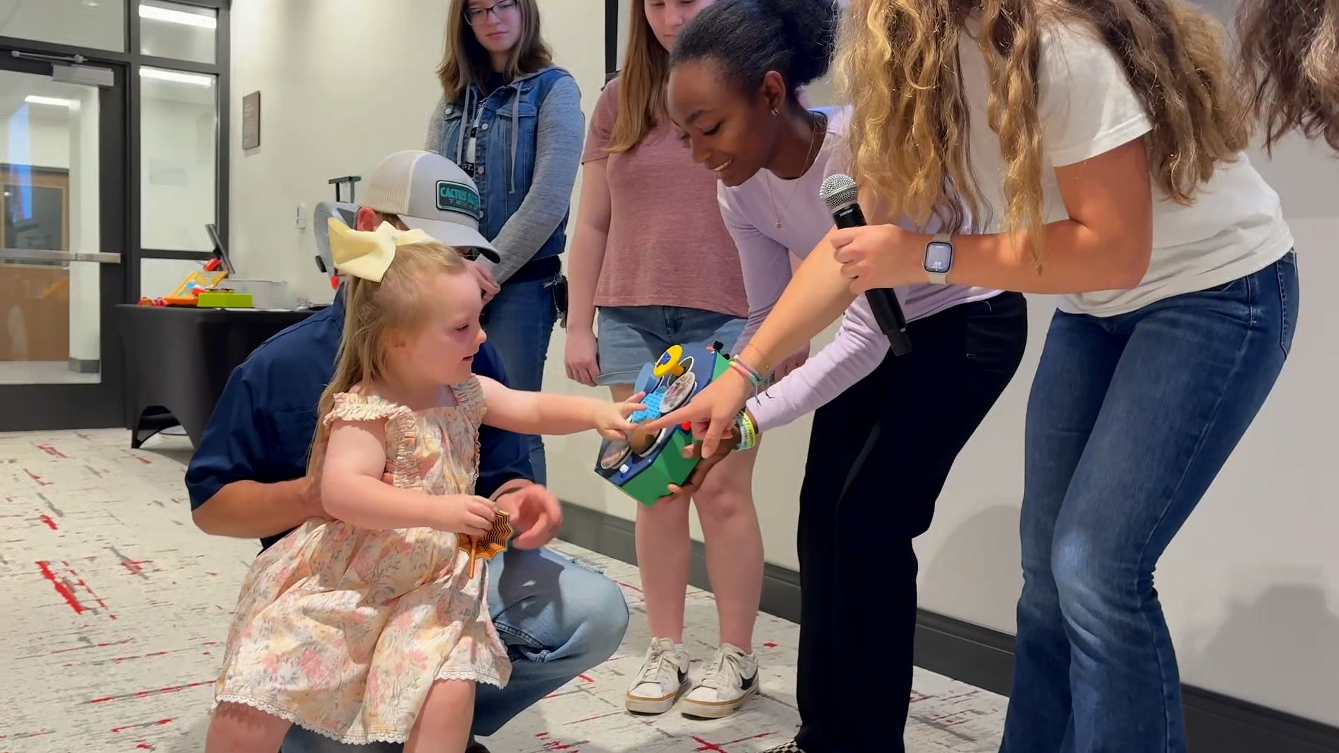 Young girl testing an interactive soundboard with assistance from a group of students.